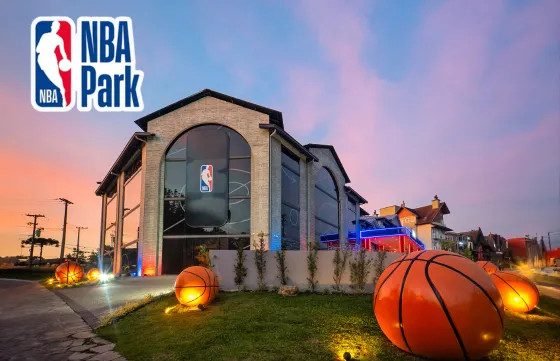 Fachada do NBA Park ao entardecer, com bolas de basquete iluminadas no jardim