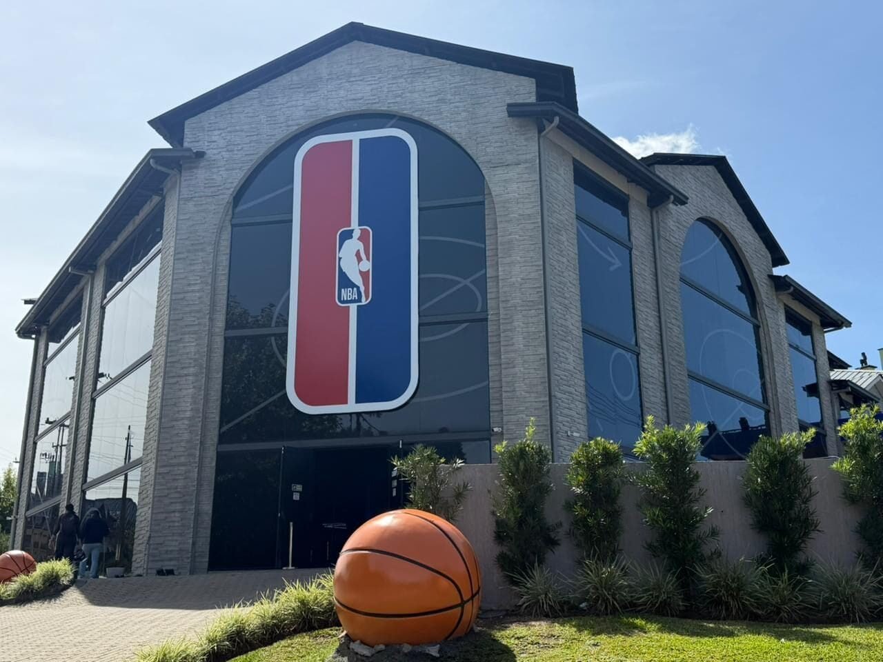 Fachada do NBA Park em Gramado, com o logo da NBA nos vidros em arco e uma grande bola de basquete decorativa no jardim